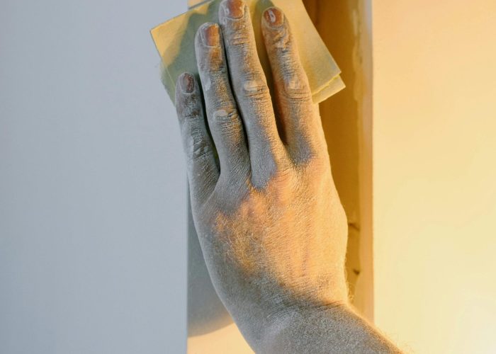 A detailed view of a person's hand sanding a wall during an indoor renovation.